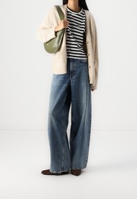 Beżowy kardigan na czarno-białej paskowanej koszuli, w połączeniu z szerokimi, niebieskimi dżinsami i brązowymi butami z noskiem w szpic. Zielona torba na ramię.