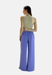 Beige mouwloze top met een ronde hals, gecombineerd met lichtpaarse, wijdvallende broek met elastische taille. Gladde stoftextuur.