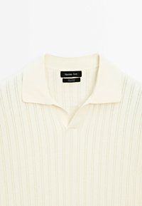 Polo en tricot de couleur crème avec des rayures verticales, un col évasé et une étiquette noire "Massimo Dutti" à l'intérieur du col.