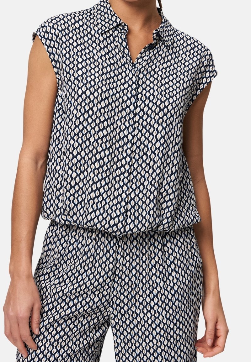 Chemise sans manches à col et pantalon assorti avec un motif géométrique bleu marine et blanc répétitif porté par une personne debout.