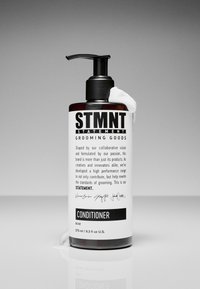 Bruine plastic fles met zwarte pompdispenser. Wit etiket met vetgedrukte zwarte tekst 'STMTNT CONDITIONER.' Gladde textuur, inhoud 275 ml.