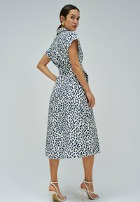 Šaty střední délky s bílou látkou a námořnickomodrým abstraktním vzorem, krátkými rukávy, přiléhavým pasem a splývavou sukní.