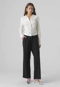 Chemise blanche à boutons avec une coupe ajustée, associée à un pantalon noir à jambes larges avec une ceinture blanche. Des escarpins argentés à bout pointu complètent le look.