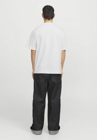 Camiseta blanca de algodón de manga corta, combinada con jeans de mezclilla oscura de corte recto, con costuras claras y dobladillos remangados.