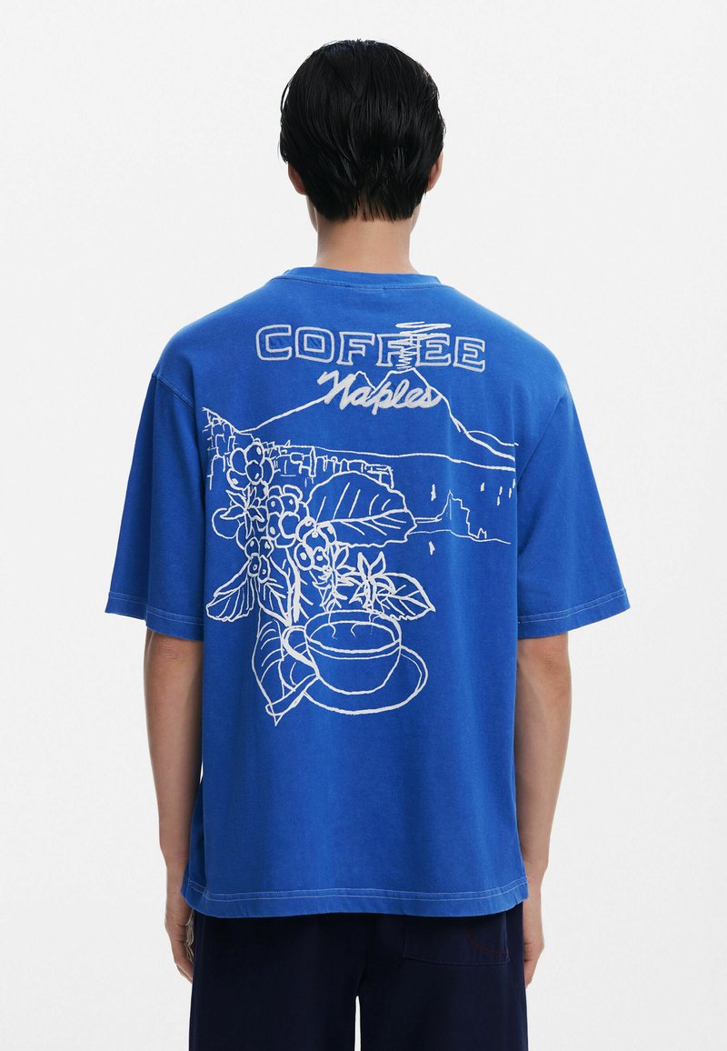 Mėlynas medvilninis marškinėlis su baltu grafiniu dizainu, vaizduojančiu kavos puodelį ir gėles, su užrašu "COFFEE Naples" ir kalnų kontūru nugarėlėje.
