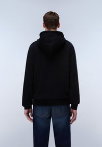 Schwarzer Kapuzenpullover mit Kängurutasche, kombiniert mit dunkelblauen Jeans mit heller Naht auf den Gesäßtaschen.