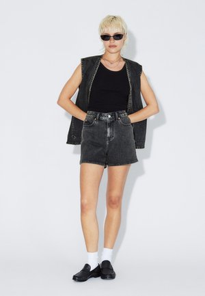 Černá denimová vesta, přiléhavé černé tílko, černé denimové kraťasy s vysokým pasem a černé nazouvací boty s bílými ponožkami. Jednoduchý, ležérní design.