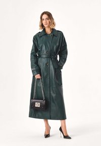 Hosszú zöld bőrkabát övvel a deréknál, nagy gallérral és gombos díszítéssel. Fekete kézitáskával párosítva, amely ezüst csattal rendelkezik.
