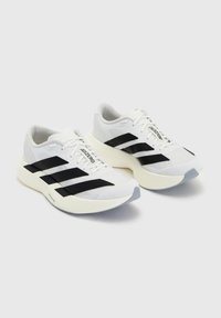 Paire de chaussures de course Adidas Adizero blanches avec des bandes noires et des semelles épaisses couleur blanc cassé sur un fond clair uni.
