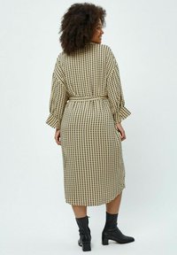 Zwart en beige gestippelde jurk met een ceintuur in de taille en wijde mouwen, reikend tot halverwege de kuit, gecombineerd met zwarte enkellaarsjes.