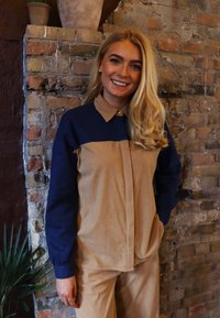 Barna és tengerészkék kordbársony ing gombos záródással, hosszú ujjakkal és galléros nyakkal. Vertikális kétszínű mintázattal és sima tapintású textúrával rendelkezik.