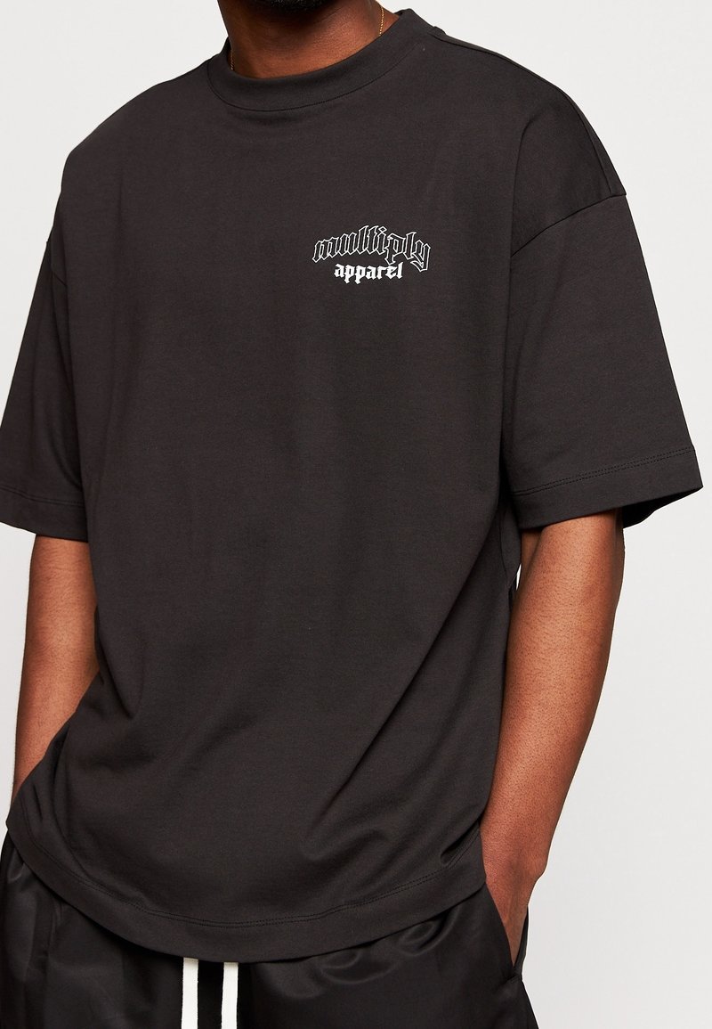 T-shirt en coton noir à coupe ample, encolure ronde et manches courtes. Présente un texte graphique blanc sur la poitrine gauche.
