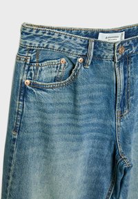 Svijetloplave traperice s izbljedjelim pranjem, dizajnom s pet džepova, bakrenom opremom i vidljivim šavovima duž struka i džepova.