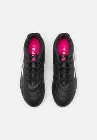 Zapatillas deportivas negras con parte superior sintética texturizada, que presentan un diseño de cordones y franjas blancas en los lados. Forro interior rosa.