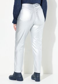 Pantalones metálicos plateados con un diseño ajustado, dos bolsillos traseros y una textura suave, combinados con botines negros.