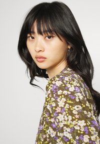 Blusa floral em castanho com flores roxas, cor-de-rosa e amarelas; tecido leve; com um decote redondo e mangas fluidas.