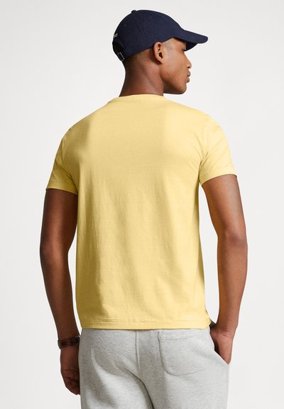 Κίτρινο βαμβακερό μπλουζάκι με κοντά μανίκια και στρογγυλή λαιμόκοψη, φορεμένο με γκρι φόρμα. Απλός σχεδιασμός με μονή υφή.