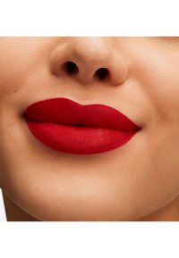 Rouge à lèvres mat rouge vif sur des lèvres lisses, présentant une forme classique et des contours définis. La couleur de la peau semble uniforme et naturelle.