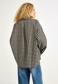 Sort og beige gingham-stribet skjorte med løs pasform og sænkede skuldre, med en klassisk krave og sideskydninger, parret med lyseblå jeans.