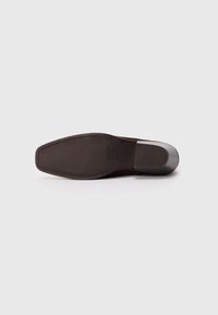 Suela de zapato de cuero marrón con forma rectangular, superficie texturada y un ligero brillo. Presenta un tacón estrecho y bordes curvados.
