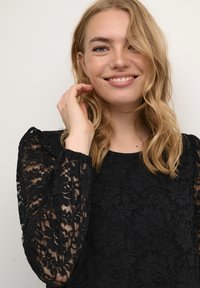 Top din dantelă neagră, cu modele florale, manșete lungi transparente și guler rotund. Material texturat cu manșete gathered și croială clasică.