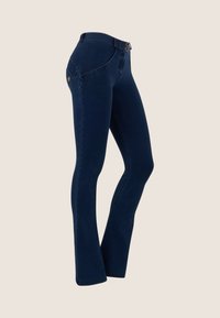 Tummansiniset istuvat farkut, joissa on keskikorkea vyötärö, kaksinappinen suljenta ja lievä levennys lahkeensuussa, esillä neutraalilla taustalla.