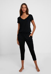 Zwart loungewear set bestaande uit een kort mouw V-hals top en cropped broeken met een elastische tailleband en zijzakken. Zachte stofstructuur.
