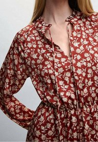 Rotes gemustertes Kleid mit langen Ärmeln, Blumendruck in Creme und dezenten Kragenverzierungen. Weicher Stoff mit Kordelzug taille.