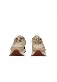 Beżowe zamszowe trampki z fakturowanymi sznurowadłami, grubą białą podeszwą i brązową gumową podeszwą zewnętrzną. Z czarnym akcentem na pięcie i nazwą marki na języku.
