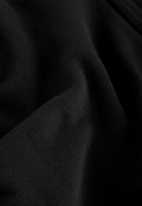 Tessuto di cotone nero con una texture liscia, caratterizzato da pieghe morbide e una leggera elasticità. La superficie appare uniforme e leggermente riflettente.