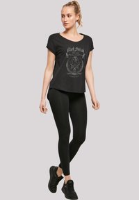 Zwarte graphic t-shirt met ronde hals en korte mouwen, met een bandlogo in het grijs. Gecombineerd met zwarte leggings en zwarte sportschoenen.
