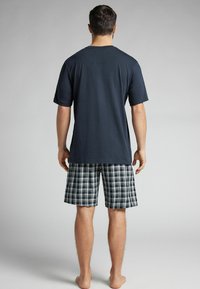 Camiseta de algodón azul marino de manga corta combinada con pantalones cortos de cuadros en tonos azul, blanco y verde, mostrando un patrón a cuadros.
