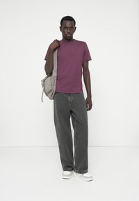 Bordo majica s round-neck izrezom, labavi sivi traperice, siva torba preko ramena i bijele tenisice. Glatka tkanina s opuštenim fitom. Jednostavan dizajn.