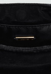 Unutrašnjost crne platnene torbe s glatkom teksturom, zlatnim hardverskim oznakama i finim šavovima duž rubova.