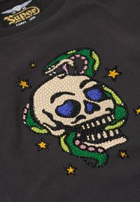 Camiseta negra con un gran gráfico de calavera colorido adornado con gemas en azul, verde, rosa y amarillo sobre una superficie texturizada.