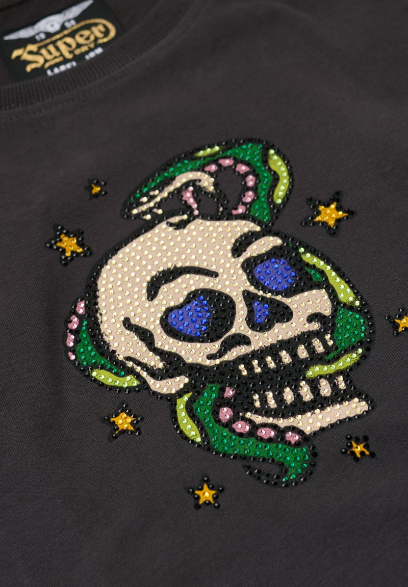 Czarny t-shirt z dużą, kolorową grafiką czaszki ozdobioną klejnotami w odcieniach niebieskiego, zielonego, różowego i żółtego na teksturowanej powierzchni.