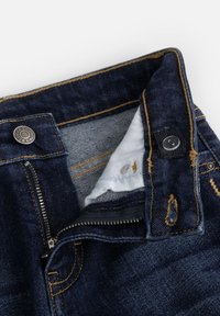 Ciemnoniebieskie dżinsy z zamkiem błyskawicznym i zapięciem na guzik, z żółtym przeszyciem i miękką podszewką. Ozdobione delikatnymi akcentami.