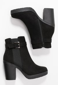 Botines de ante negro con un tacón grueso, que cuentan con un cierre lateral, panel elástico y un acento decorativo de hebilla.