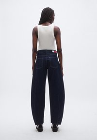 Tumedasinised laia lõikega teksad, valmistatud denimist, millel on kõrge vöökoht, klassikalised tagataskud ja kaubamärgiga silt vöörihmal.