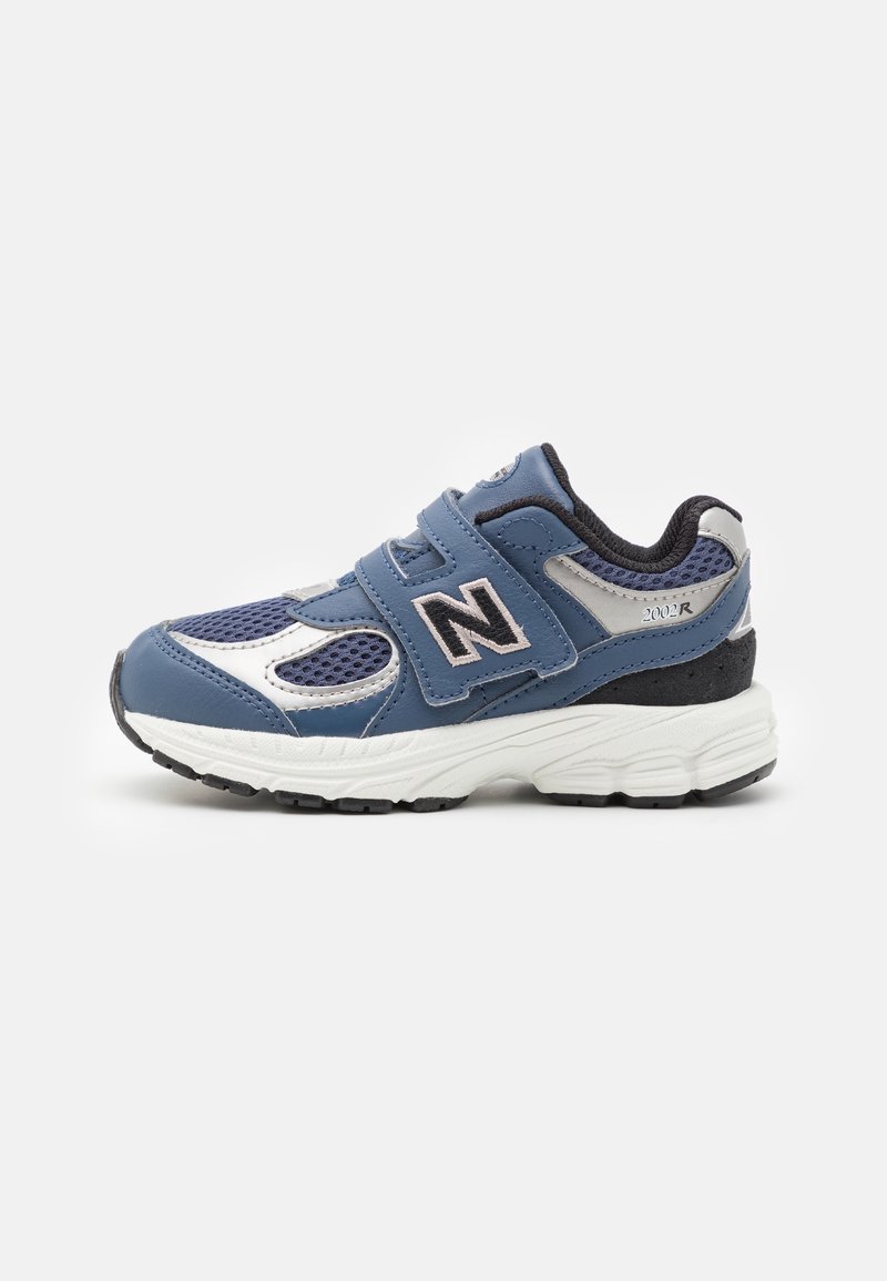 Baskets New Balance bleu et blanc avec bandes Velcro, doublure intérieure noire et semelle blanche épaisse, montrées de profil sur un fond uni.