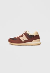 Smeđi i bež New Balance tenisice s panelima od antilopa i mreže, bijelim vezicama i bež gumenom potplatom na jednostavnoj svijetlosivoj pozadini.