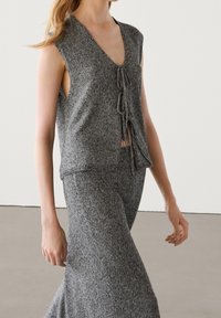 Gray knit vest with a deep V-neck and short sleeves, featuring a tie fastening at the front. Paired with a matching gray skirt.