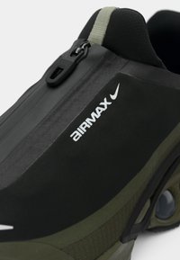 Juodos ir alyvinės žalios spalvos Nike Air Max bateliai, turintys elegantišką, vandeniui atsparų paviršių, užtrauktuko užsegimą ir ryškų baltą logotipą šone.