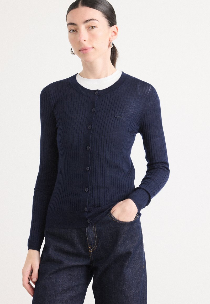 Marinblå ribbad cardigan med långa ärmar och knappstängning, med en rund halsringning och en liten logodetalj på bröstet.