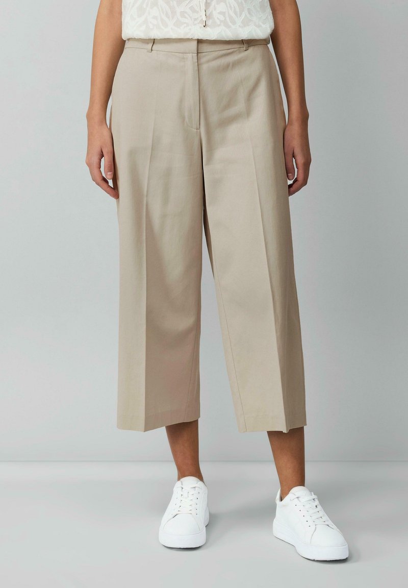 Beige wijde broek met plooien, voorzien van een gladde textuur en zijzakken, gecombineerd met witte sneakers.