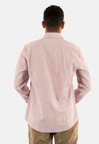 Lange mouwen shirt in lichtroze met een gestructureerd patroon. Voorzien van een standaardkraag en knopenmanchetten. De achterkant laat een afgeronde zoom en een yoke-ontwerp zien.