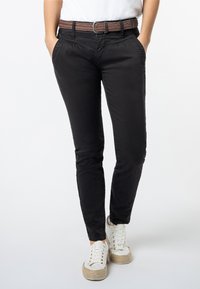 Zwarte slim-fit broek van zachte stof, met een gevlochten bruine riem en zijzakken, gecombineerd met witte sneakers met jute-accenten.