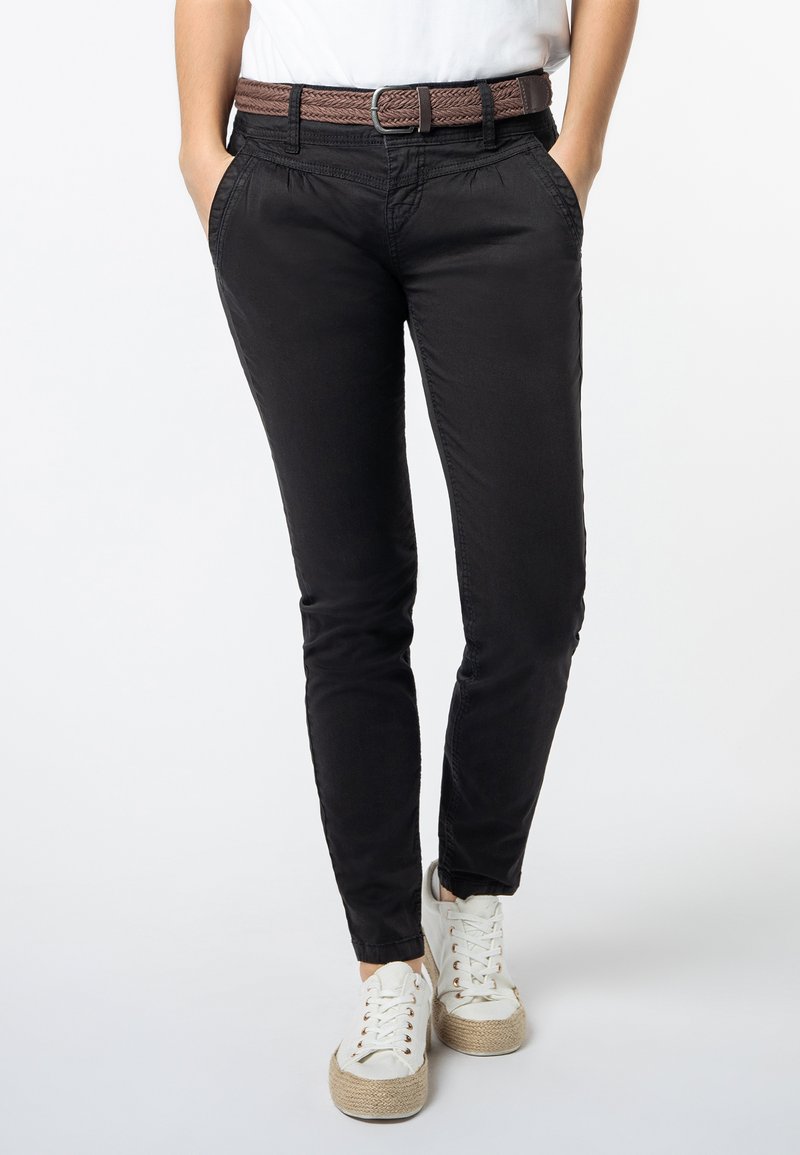Zwarte slim-fit broek van zachte stof, met een gevlochten bruine riem en zijzakken, gecombineerd met witte sneakers met jute-accenten.