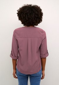 Blusa color lampone con maniche a tre quarti e polsini arrotolati, dotata di una plica sul retro e una trama di tessuto liscia.