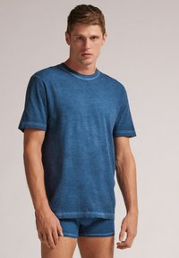 Blaues Baumwoll-T-Shirt mit kurzen Ärmeln und rundem Ausschnitt, mit einer leicht verblassten Textur und passenden blauen Shorts.